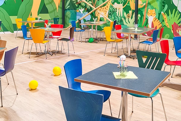 Ein Restaurant in Augsburg mit bunten Tischen und Stühlen, einem Indoor-Spielplatz und einem Dschungelthema.